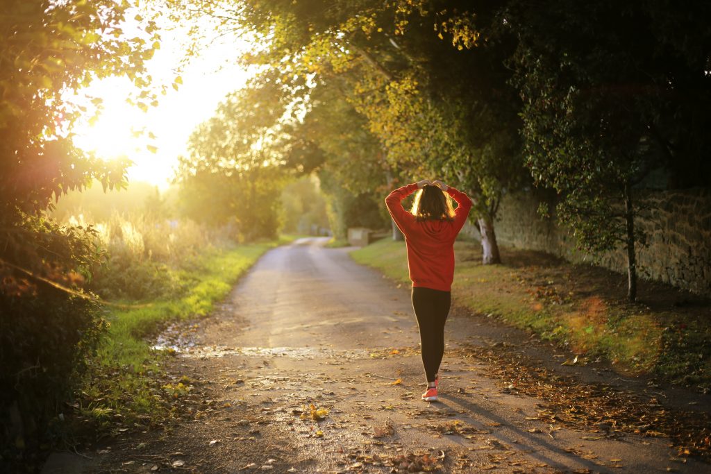 A photo of a woman walking outdoors, her back to the viewer and arms raised above her head