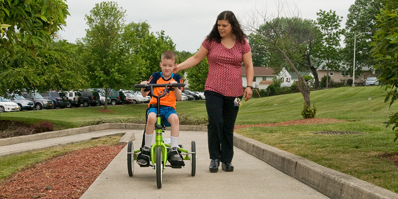 Physical Therapist walking alongside pediatric patient on a bike outside