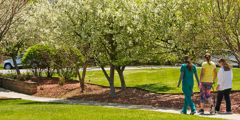 Female patient walking outdoors with cane and physical therapist and assistant