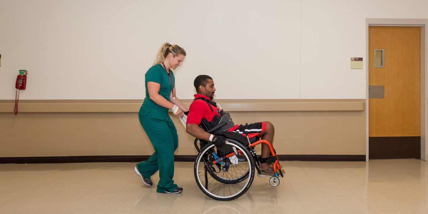 Nurse assisting patient in wheelchair down a hallway